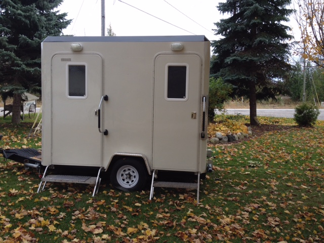 A portable toilet sitting in the grass near some trees.